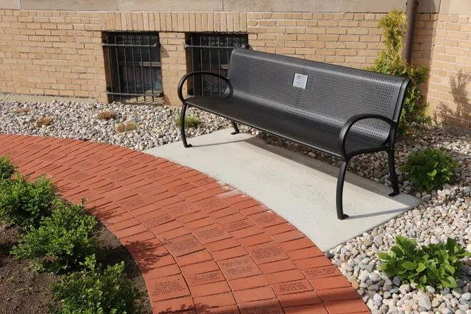 Mid-shot view of engraved red brick pavers in front of bench, situated around flagpole outside the Adrian Armory