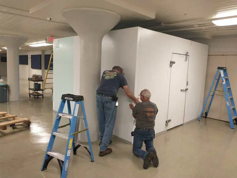 Two men working on installing a walk-in cooler for the community kitchen at the Adrian Armory.